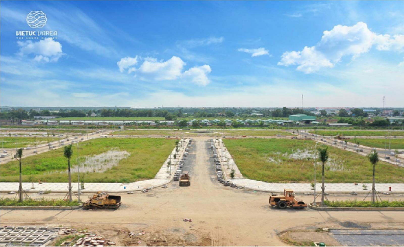 Ảnh chụp một con đường đang trong quá trình thi công với máy san, ủi đất. Xung quanh có nhiều bãi đất trống