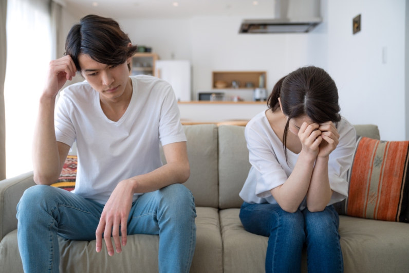 Hình ảnh người đàn ông ngồi chống tay lên đầu mặt buồn rầu, còn người phụ nữ cúi mặt ôm đầu