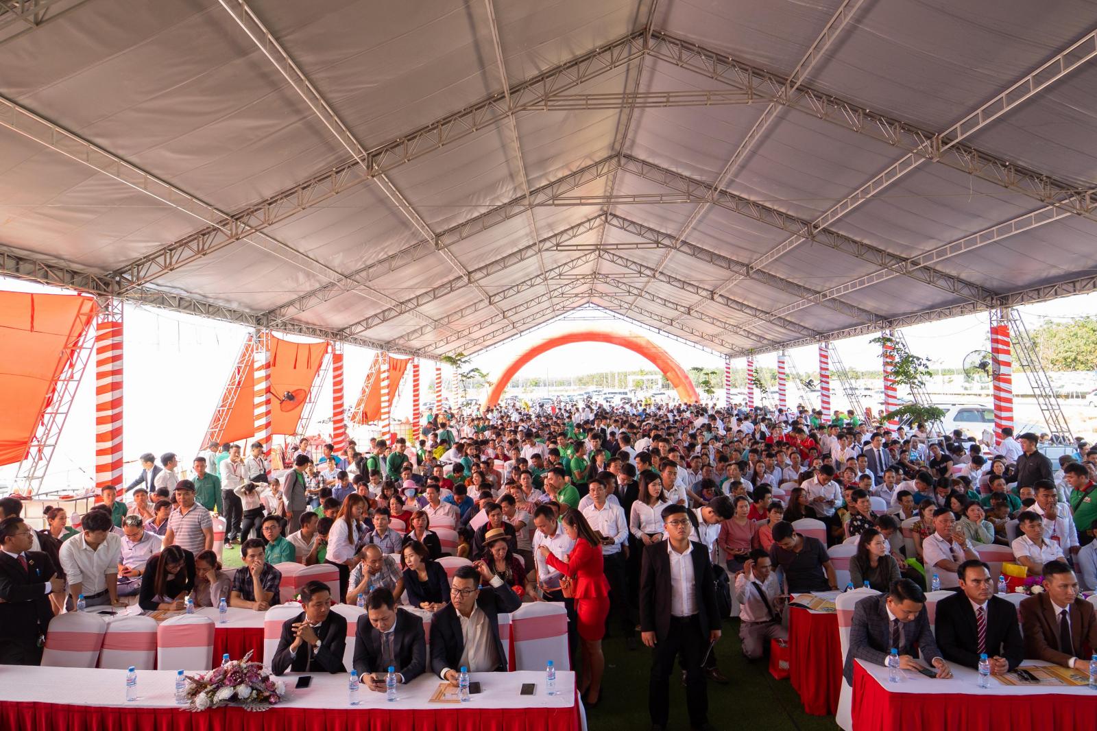 Rất nhiều người đang ngồi tham gia một sự kiện tổ chức ngoài trời có mái che 
