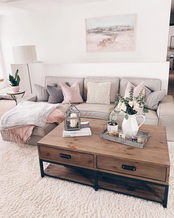 H&igrave;nh ảnh một g&oacute;c ph&ograve;ng kh&aacute;ch m&agrave;u be chủ đạo với sofa ghi x&aacute;m, gối tựa m&agrave;u hồng phấn, b&agrave;n tr&agrave; gỗ, ph&iacute;a tr&ecirc;n đặt b&igrave;nh c&acirc;y xanh sinh động