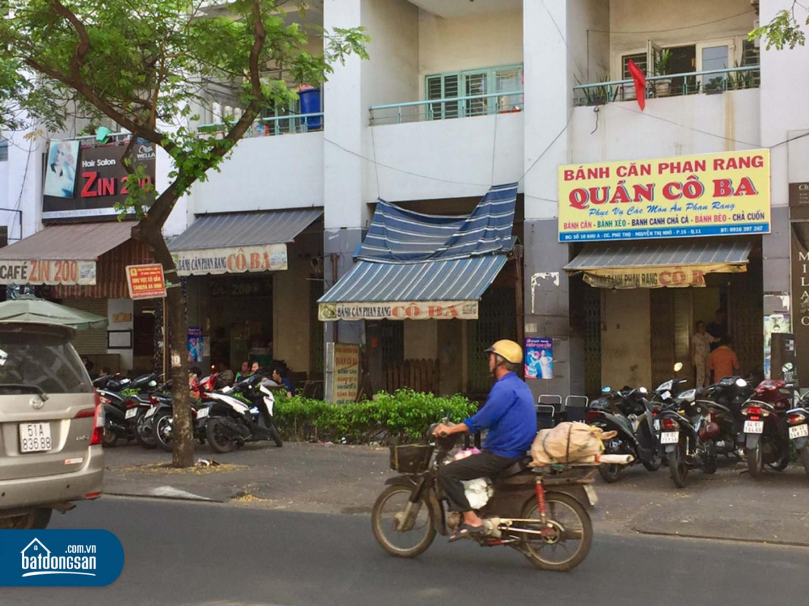 Dãy shophouse treo biển bán hàng cạnh một con đường, trên vỉa hè dựng nhiều xe máy.