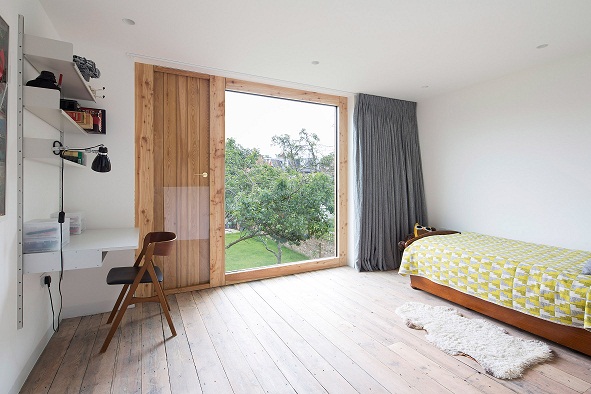 H&igrave;nh ảnh to&agrave;n cảnh ph&ograve;ng ngủ rộng r&atilde;i, tho&aacute;ng s&aacute;ng với s&agrave;n l&aacute;t gỗ, ga gối m&agrave;u xanh l&aacute;, kệ mở gắn tường, cửa k&iacute;nh lớn.