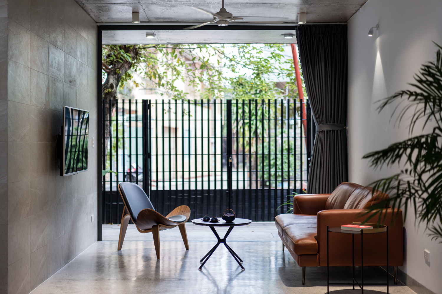 H&igrave;nh ảnh to&agrave;n cảnh ph&ograve;ng kh&aacute;ch với tường b&ecirc; t&ocirc;ng x&aacute;m, ghế sofa m&agrave;u v&agrave;ng da b&ograve;, c&acirc;y xanh trang tr&iacute;