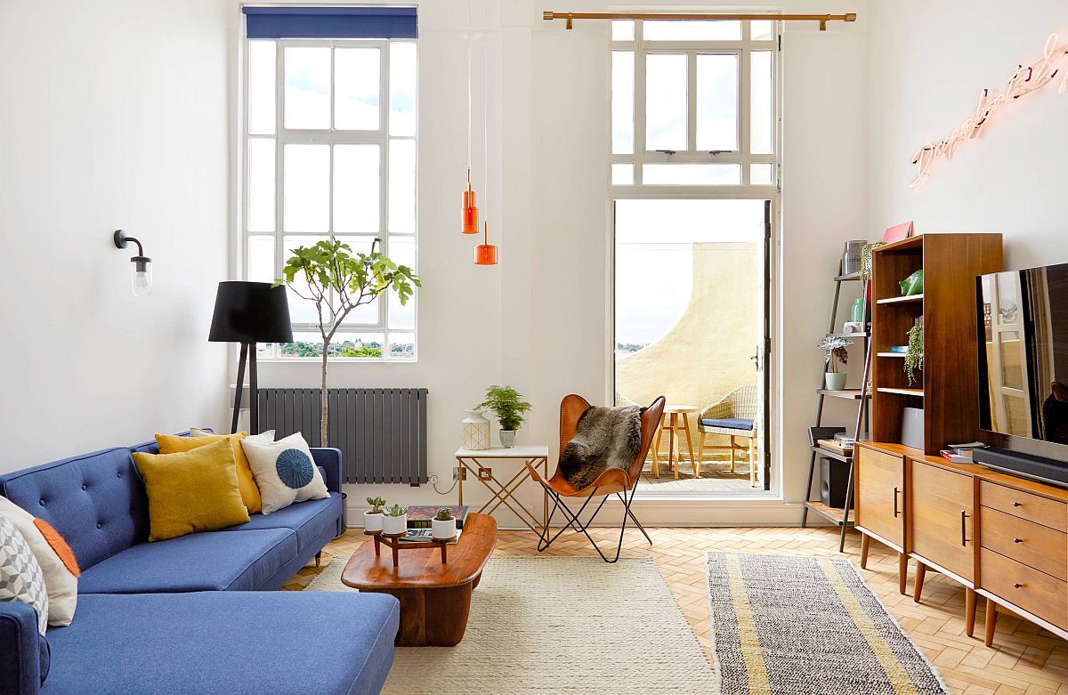 H&igrave;nh ảnh to&agrave;n cảnh ph&ograve;ng kh&aacute;ch nhỏ với sofa m&agrave;u xanh lam, b&agrave;n tr&agrave; gỗ, đối diện l&agrave; tủ kệ tivi c&oacute; ngăn k&eacute;o, cửa sổ k&iacute;nh trong suốt