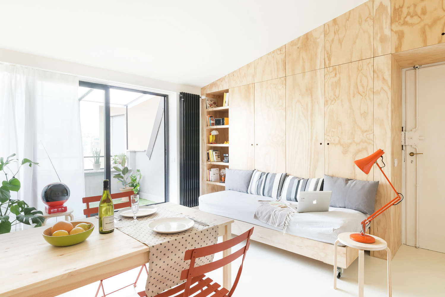 Hình ảnh góc tiếp khách với sofa ghi xám liền kề với bàn ăn, đèn màu cam tạo điểm nhấn bắt mắt