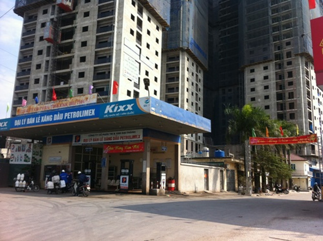 Tòa nhà chung cư cao tầng đang xây dựng, bên dưới là trạm xăng dầu nằm gần con đường lớn.