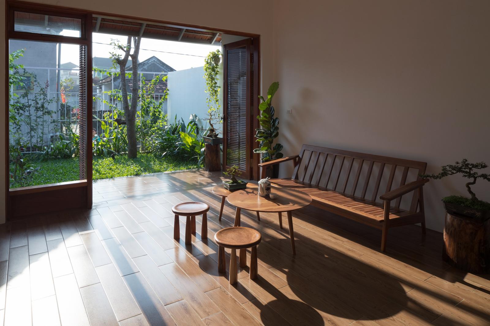 Phòng khách tràn ngập ánh nắng Hình ảnh phòng khách ngập tràn ánh nắng với sofa gỗ, bàn trà tròn, cửa lớn mở ra sân vườn