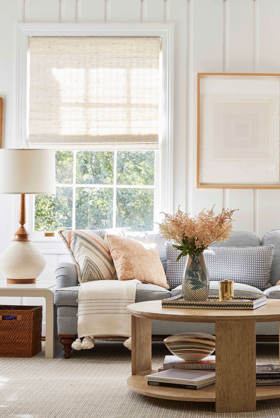 Hình ảnh một góc phòng khách với sofa xám, gối tựa màu sắc, bàn trà gỗ tròn, cửa sổ kính
