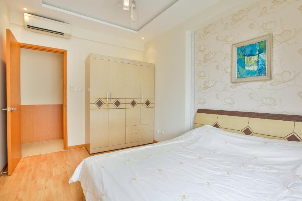 Hình ảnh phòng ngủ ông bà tông màu trắng sáng với giấy dán tường hoa văn nổi sang trọng,tranh treo màu xanh dương, tủ quần áo cùng tông với giường, cửa ra vào đang mở.