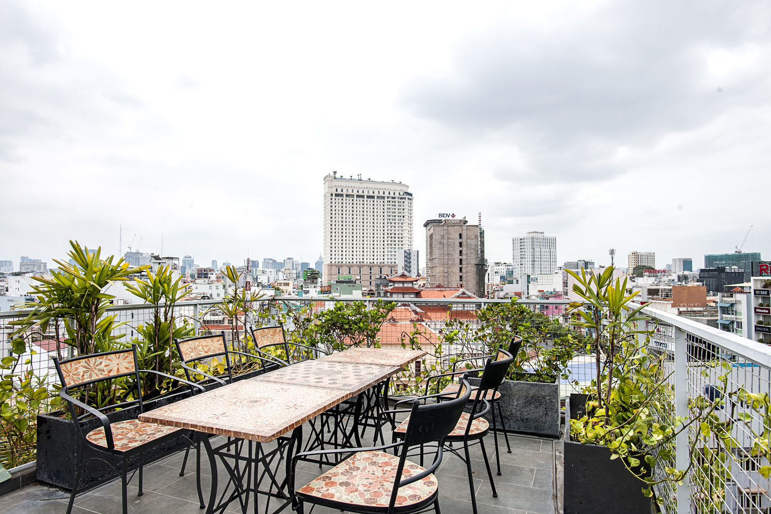 Hình ảnh cận cảnh sân thượng nhà phố 7 tầng với bộ bàn ghế thư giãn, cây xanh bao quanh, lan can lưới an toàn