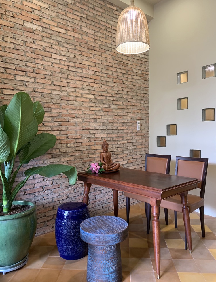 Góc bàn ăn mộc mạc, sử dụng nội thất gỗ chủ đạo Hình ảnh một góc bàn ăn với bàn gỗ, tường gạch nung không sơn trát, đôn ngồi bằng gốm xanh, chậu chuối cảnh trang trí