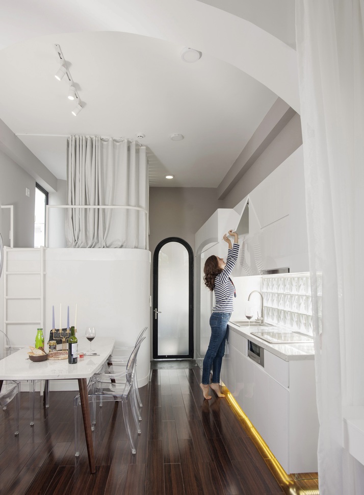 Phòng bếp ăn phong cách Paris Hình ảnh phòng bếp ăn phong cách Paris với bàn đá màu trắng, sàn lát gỗ bóng, người phụ nữ đang với tay mở cửa tủ bếp trên