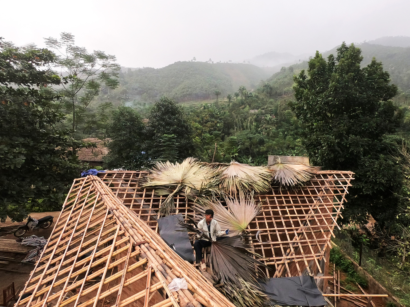 Hình ảnh một người đàn ông đang lợp mái nhà bằng lá