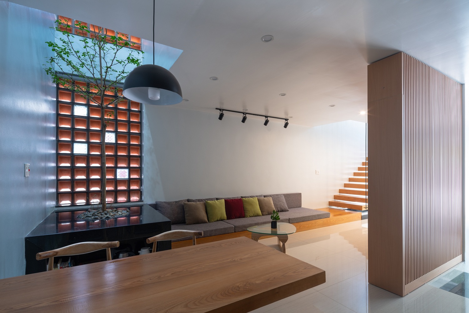 H&igrave;nh ảnh ph&ograve;ng kh&aacute;ch ấn tượng với bồn c&acirc;y xanh t&ocirc;n cao ngay dưới giếng trời, ghế sofa k&eacute;o d&agrave;i từ bậc ch&acirc;n cầu thang
