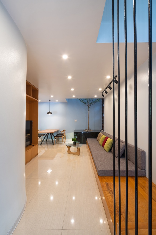 Hình ảnh phòng khách nhà phố nhìn từ lối vào với sofa xám, gối tựa màu sắc, bồn cây lớn