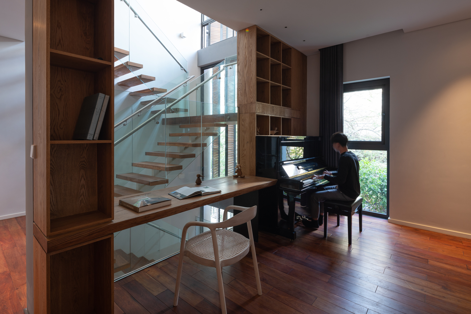 H&igrave;nh ảnh g&oacute;c l&agrave;m việc v&agrave; thư gi&atilde;n cạnh cửa sổ k&iacute;nh tho&aacute;ng s&aacute;ng với đ&agrave;n piano, b&agrave;n gỗ, tường k&iacute;nh