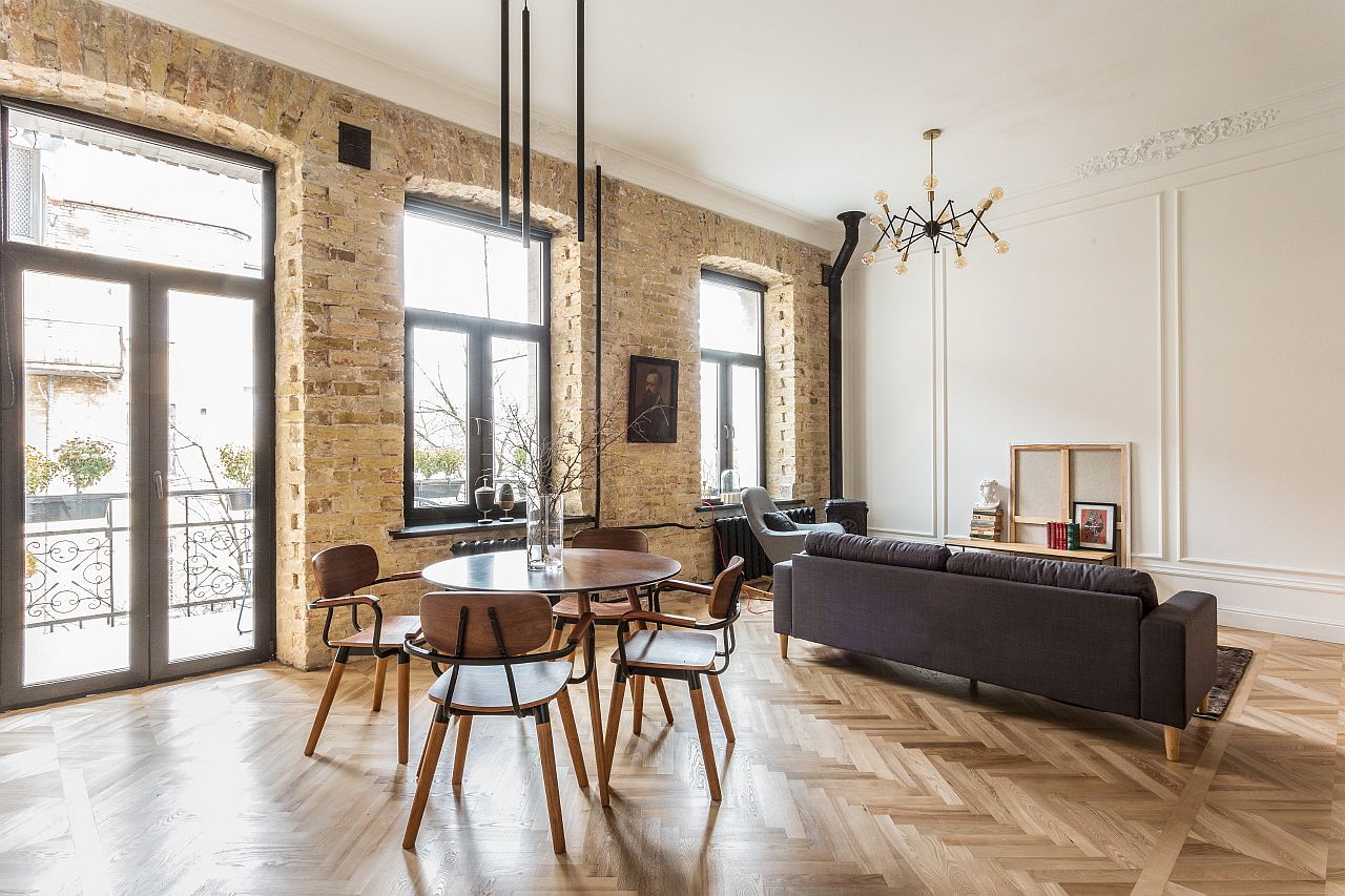 h&igrave;nh ảnh to&agrave;n cảnh ph&ograve;ng kh&aacute;ch v&agrave; ph&ograve;ng ăn trong căn hộ hiện đại với b&agrave;n ăn tr&ograve;n, sofa ghi x&aacute;m, tường gạch th&ocirc;, cửa sổ k&iacute;nh