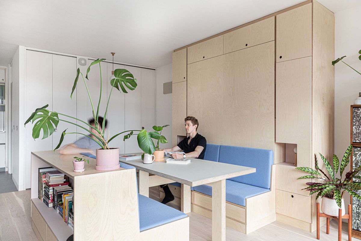 h&igrave;nh ảnh ph&ograve;ng ăn trong căn hộ studio nhỏ ở London với b&agrave;n ghế gỗ l&oacute;t nệm m&agrave;u xanh, hai ch&agrave;ng trai trẻ