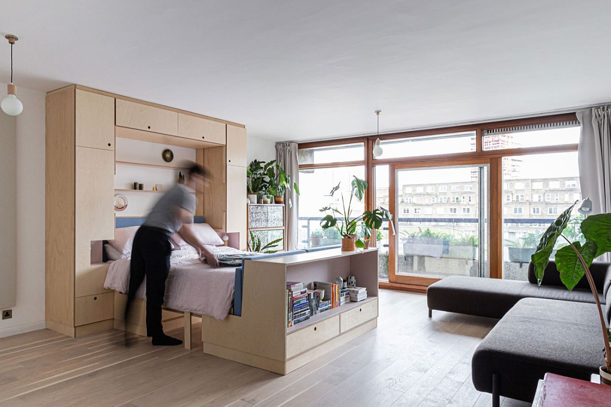 h&igrave;nh ảnh to&agrave;n cảnh kh&ocirc;ng gian sinh hoạt trong căn hộ nhỏ ở London với ghế sofa m&agrave;u ghi x&aacute;m, giường gấp, c&acirc;y xanh