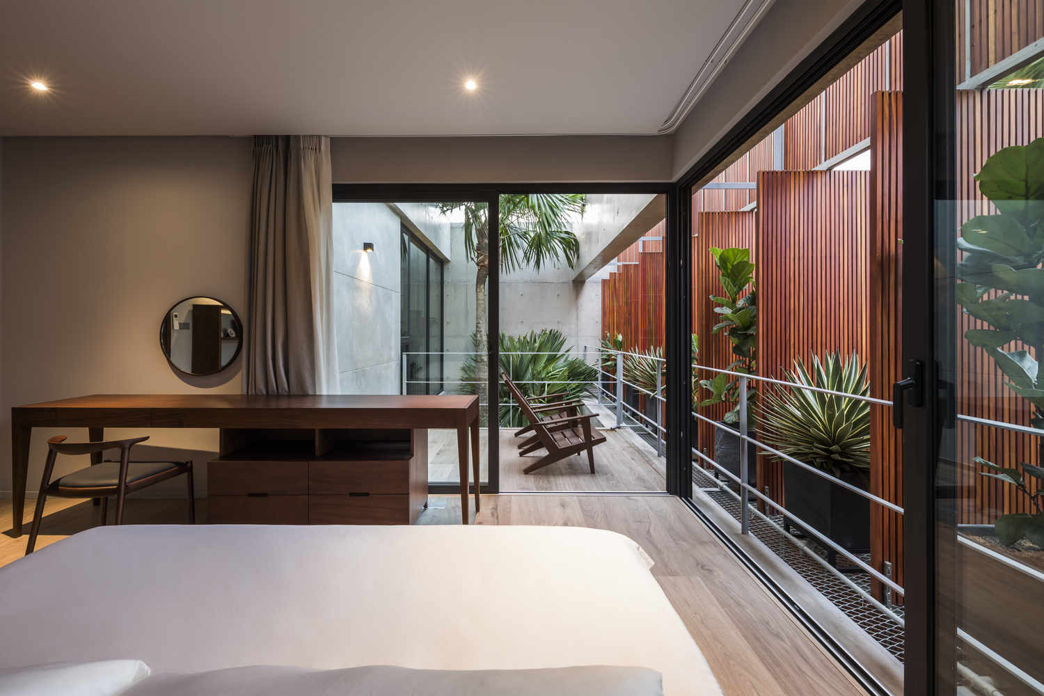 h&igrave;nh ảnh ph&ograve;ng ngủ tho&aacute;ng rộng với b&agrave;n ghế gỗ, tường k&iacute;nh, lan can sắt nh&igrave;n ra giếng trời