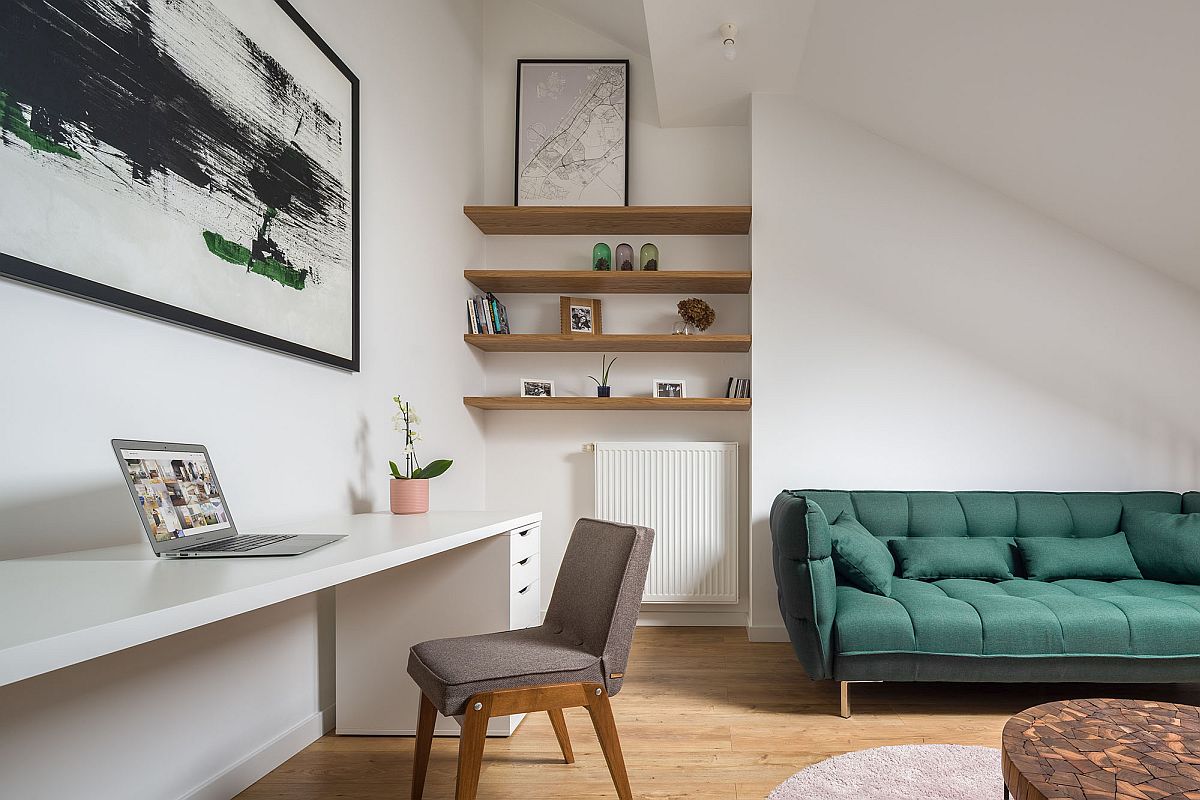 hình ảnh một góc phòng khách trên tầng lửng căn hộ nhỏ với sofa màu xanh lá, góc làm việc gọn gàng, tranh treo tường trừu tượng