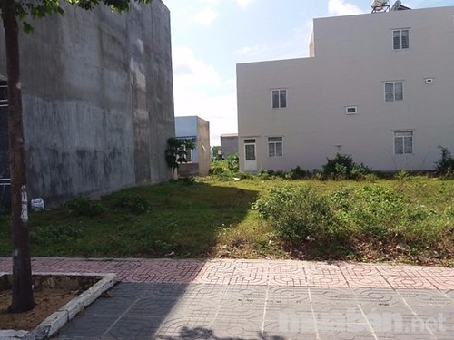 Một mảnh đất trống, bên cạnh là một ngôi nhà cao tầng