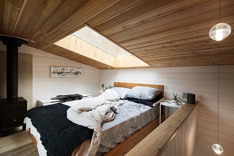 h&igrave;nh ảnh to&agrave;n cảnh ph&ograve;ng ngủ tr&ecirc;n g&aacute;c lửng nh&agrave; cabin gỗ ở Canada với cửa sổ k&iacute;nh tr&ecirc;n m&aacute;i, giường nệm &ecirc;m &aacute;i, tranh treo tường, chậu c&acirc;y đặt tr&ecirc;n b&agrave;n nhỏ đầu giường