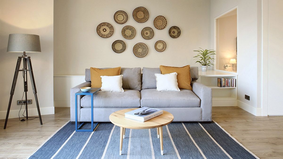 H&igrave;nh ảnh ph&ograve;ng kh&aacute;ch căn hộ nhỏ m&agrave;u trắng xanh với sofa x&aacute;m, thảm trải kẻ sọc xanh, trang tr&iacute; tường ấn tượng