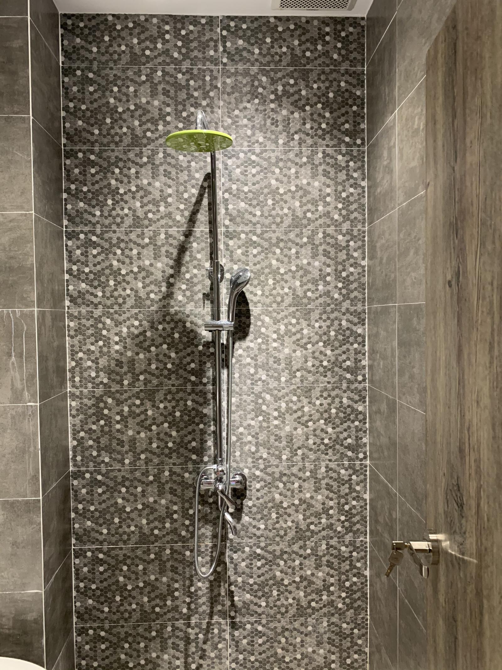Khoảng tường mosaic đá tự nhiên tạo điểm nhấn cho không gian phòng tắm thêm sang trọng. Vòi tắm hoa sen