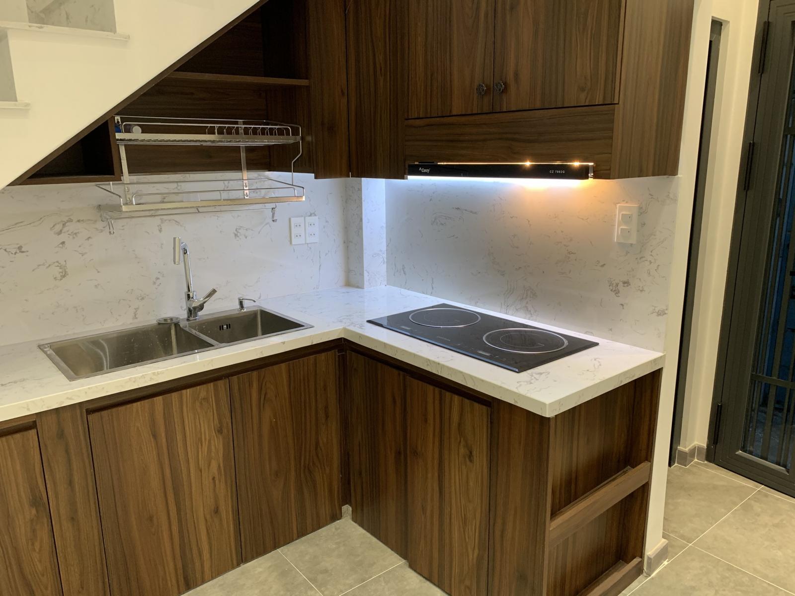 Khu bếp đã được hoàn thiện cơ bản với mặt bếp, bồn rửa, hệ thống kệ, giá bát nâng hạ Không gian bếp, mặt bếp từ, bồn rửa, tủ kệ