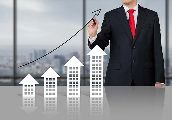 Người đ&agrave;n &ocirc;ng đứng cạnh m&ocirc; h&igrave;nh 3 ng&ocirc;i nh&agrave; v&agrave; mũi t&ecirc;n đi l&ecirc;n minh họa gi&aacute; bất động sản tăng.