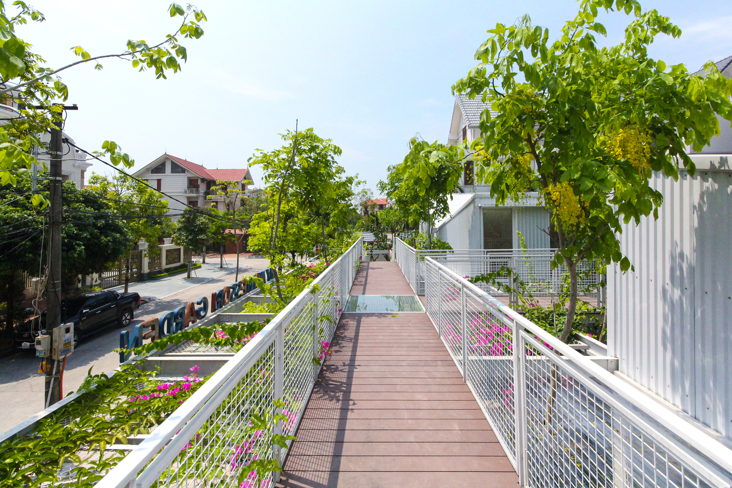 h&igrave;nh ảnh h&agrave;nh lang ngo&agrave;i trời, tầng m&aacute;i trường mầm non với s&agrave;n l&aacute;t gỗ, hai b&ecirc;n l&agrave; lan can lưới th&eacute;p m&agrave;u trắng, c&acirc;y xanh ngập tr&agrave;n