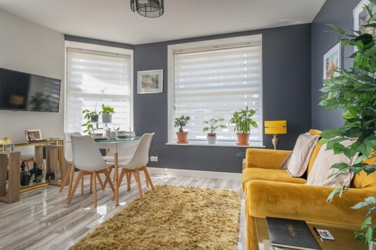 hình ảnh phòng khách liên thông khu bếp ăn với sofa màu vàng, đối diện là bộ bàn ăn nhỏ gọn, gạch giả đá lát sàn