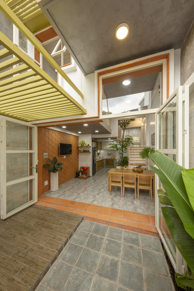 hình ảnh tầng trệt nhà mái đôi với cửa cao rộng, tường ốp gạch đỏ, bàn ăn bằng gỗ, phía trong là khu bếp nấu