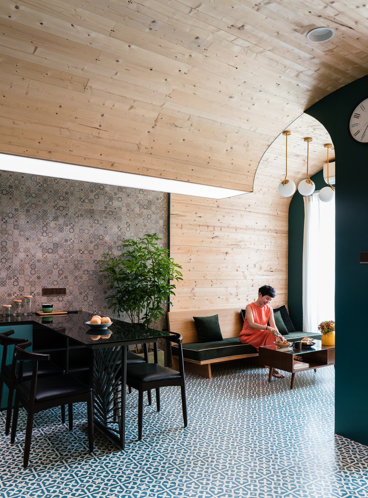 h&igrave;nh ảnh người phụ nữ mặc v&aacute;y m&agrave;u cam ngồi ở sofa ph&ograve;ng kh&aacute;ch, cạnh đ&oacute; l&agrave; b&agrave;n ăn bằng gỗ sẫm m&agrave;u