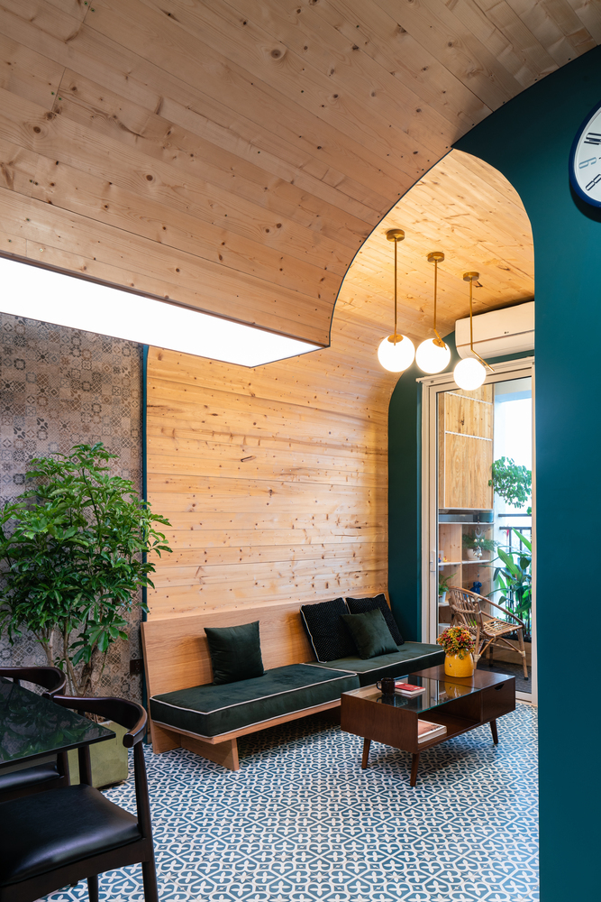 H&igrave;nh ảnh ph&ograve;ng kh&aacute;ch căn hộ nhỏ với tường v&agrave; trần v&ograve;m ốp gỗ, sofa bọc nệm m&agrave;u xanh dương, b&agrave;n tr&agrave; k&iacute;nh, bộ ba đ&egrave;n thả mặt d&acirc;y chuyền ấm &aacute;p