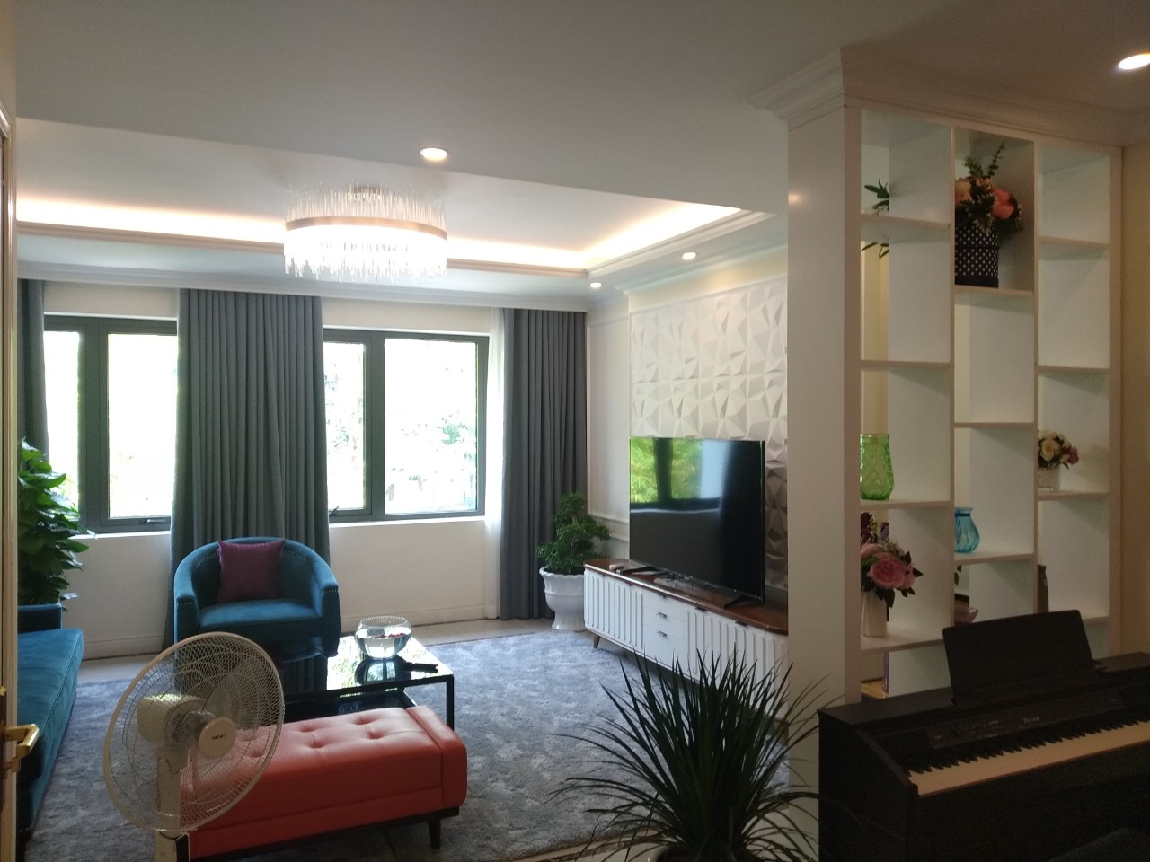 hình ảnh phòng khách biệt thự sang trọng với sofa nhung mà xanh nước biển, ghế phụ màu cam đất, đèn chùm, cạnh đó là phòng thư giãn với đàn piano