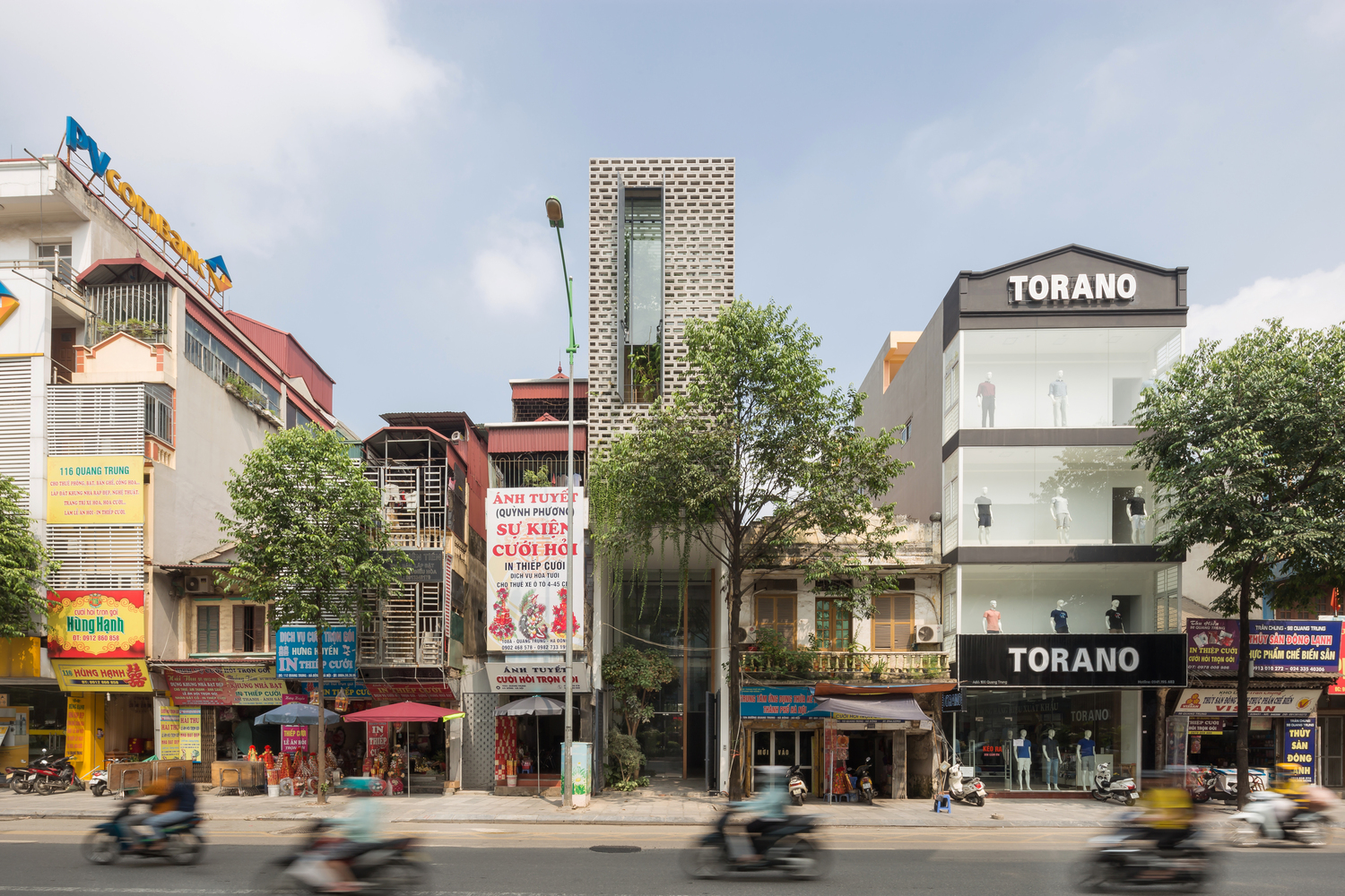 hình ảnh toàn cảnh mặt tiền ngôi nhà Việt CH House với tường gạch lỗ, cửa sổ kính chữ nhật lớn, cây xanh tạo điểm nhấn