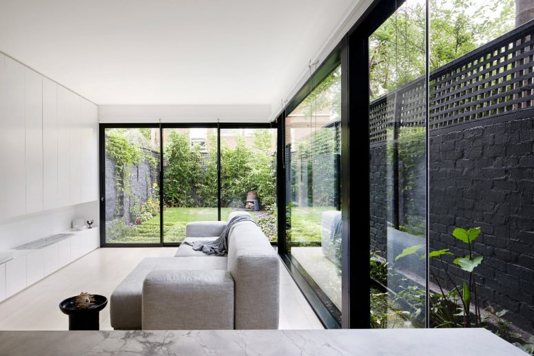 h&igrave;nh ảnh ph&ograve;ng kh&aacute;ch phong c&aacute;ch tối giản với sofa ghi s&aacute;ng, tủ kệ m&agrave;u trắng &acirc;m tường, tường v&agrave; cửa k&iacute;nh trong suốt mở ra s&acirc;n vườn