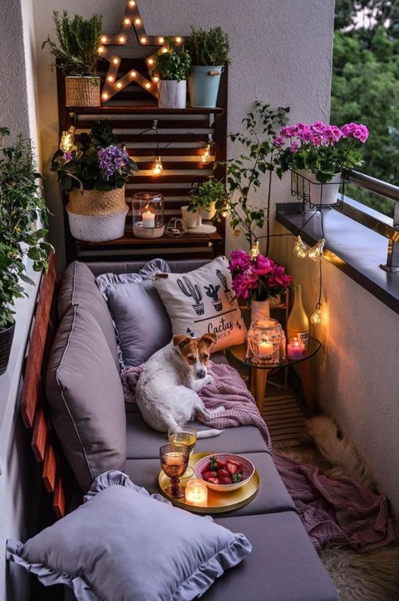 Một ban c&ocirc;ng nhỏ ấm &aacute;p với bức tường ốp gỗ pallet, ghế sofa &ecirc;m &aacute;i kết hợp h&agrave;i h&ograve;a với chậu hoa, c&acirc;y xanh v&agrave; đ&egrave;n nến.