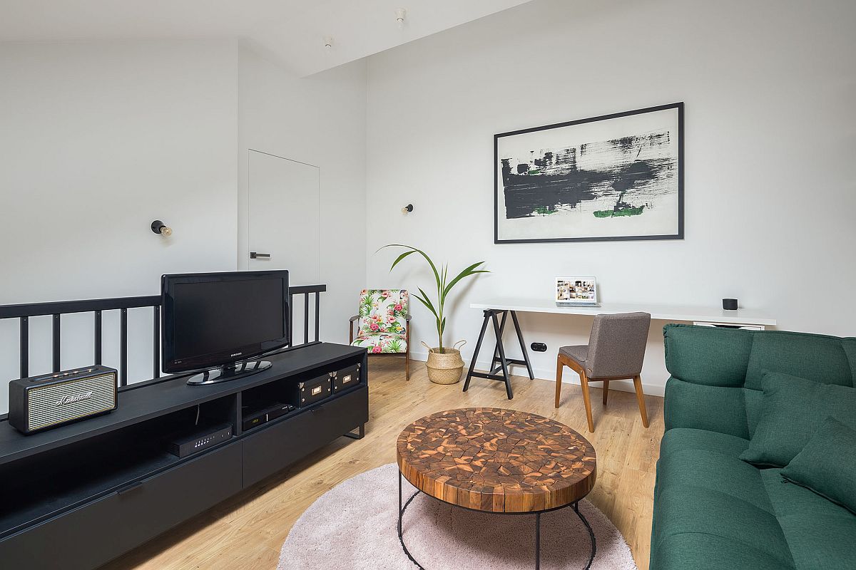 Phòng khách trên gác lửng được bài trí ấn tượng với sofa màu xanh rêu, bàn trà độc đáo và tủ kệ tivi màu đen cá tính. Cạnh đó là góc làm việc đơn giản, gọn gàng.