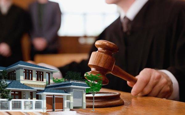 một thẩm ph&aacute;n đang ngồi x&eacute;t xử tại toa, b&ecirc;n cạnh l&agrave; m&ocirc; h&igrave;nh ng&ocirc;i nh&agrave;