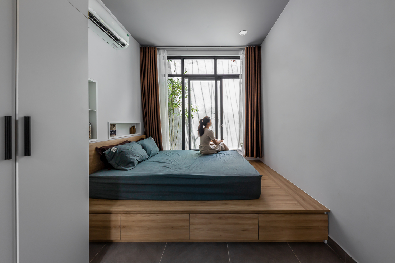 cô gái ngòi trên giường thấp sàn, nhìn ra ngoài cửa sổ