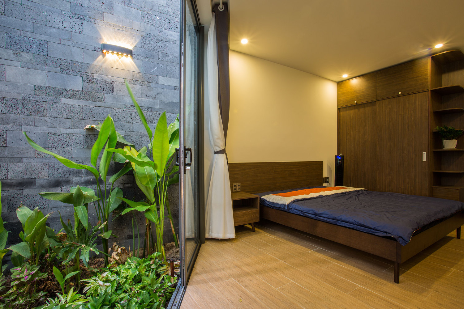 Ph&ograve;ng ngủ của vợ chồng gia chủ v&agrave; ph&ograve;ng của con nhỏ được thiết kế ở tầng 1. Hai ph&ograve;ng đều c&oacute; cửa k&iacute;nh lớn mở ra giếng trời đ&oacute;n nắng, gi&oacute;.