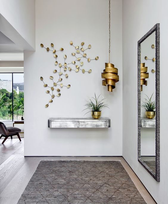 lối vào nhà với kệ bằng kim loại xám, đèn thả và chậu cây bằng đồng, phù điêu gắn tường, gương lớn hình chữ nhật
