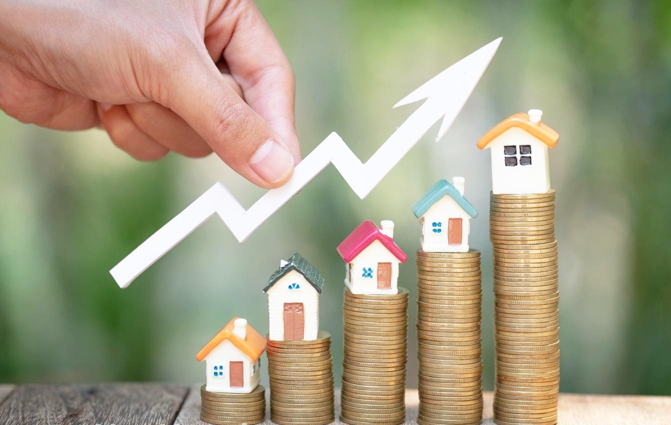 h&igrave;nh ảnh c&aacute;c cọc tiền xu theo hướng tăng dần, tr&ecirc;n đỉnh l&agrave; m&ocirc; h&igrave;nh ng&ocirc;i nh&agrave;, b&agrave;n tay cầm mũi ti&ecirc;n m&agrave;u trắng hướng đi l&ecirc;n