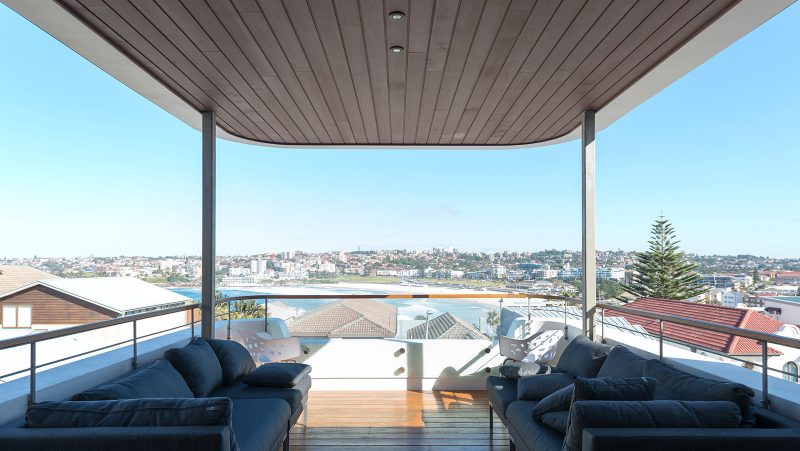 ph&ograve;ng kh&aacute;ch ngo&agrave;i trời với ghế sofa m&agrave;u xanh dương, hướng nh&igrave;n ra b&atilde;i biển Bondi