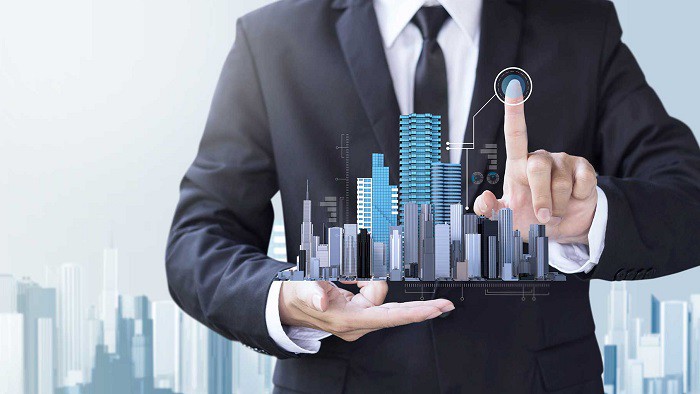 h&igrave;nh ảnh một người đ&agrave;n &ocirc;ng mặc vest m&agrave;u đen, tr&ecirc;n tay l&agrave; m&ocirc; h&igrave;nh ng&ocirc;i nh&agrave; cao tầng, đ&ocirc; thị