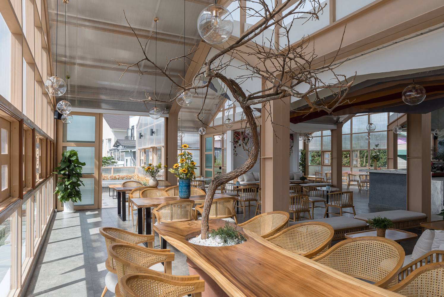 h&igrave;nh ảnh b&ecirc;n trong qu&aacute;n c&agrave; ph&ecirc; ở Đ&agrave; Lạt với b&agrave;n ghế m&acirc;y tre đan, đ&egrave;n thả sợi đốt, cửa sổ k&iacute;nh ngập tr&agrave;n &aacute;nh s&aacute;ng