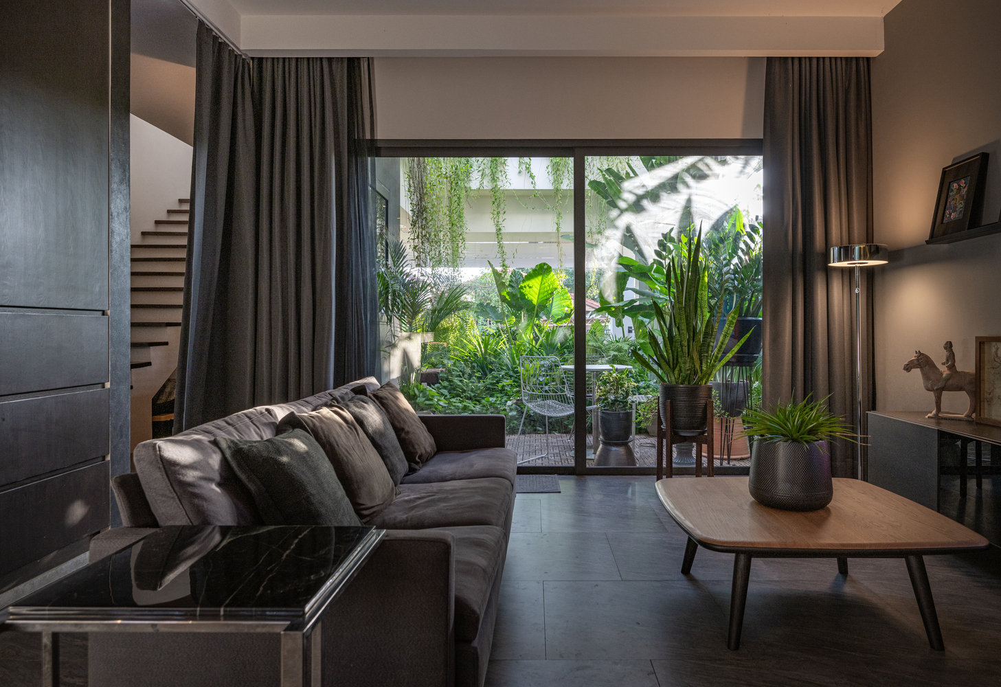 ph&ograve;ng kh&aacute;ch biệt thự với cửa k&iacute;nh lớn nh&igrave;n ra s&acirc;n vườn, sofa da n&acirc;u, r&egrave;m cửa m&agrave;u đen